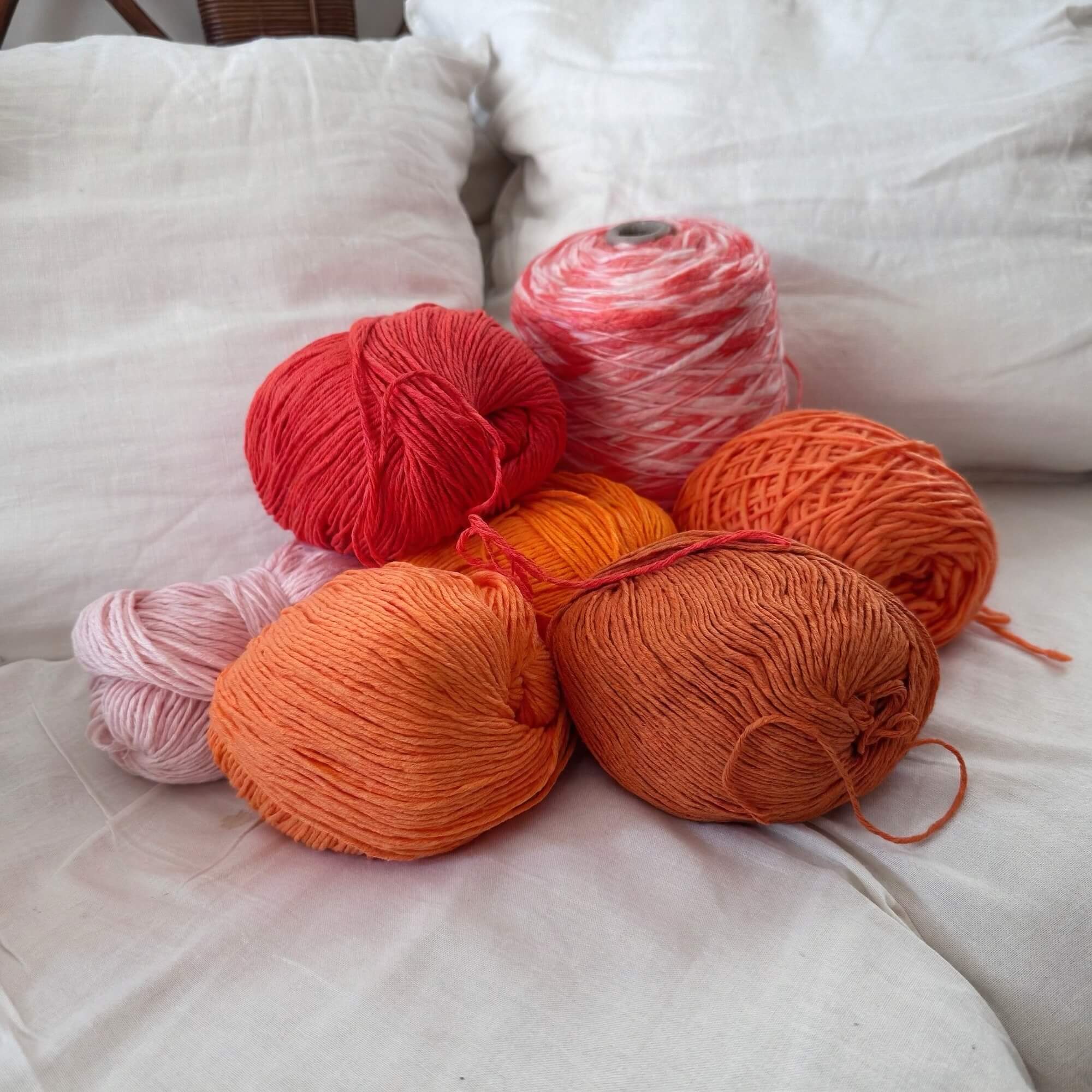 Assorted skeins of yarn in red, pink, and orange on a white surface